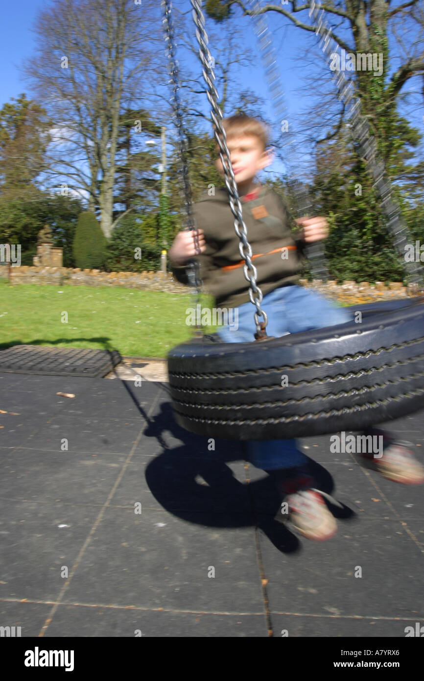 Ragazzo giocando sul parco giochi tire swing sfocatura del movimento Foto Stock