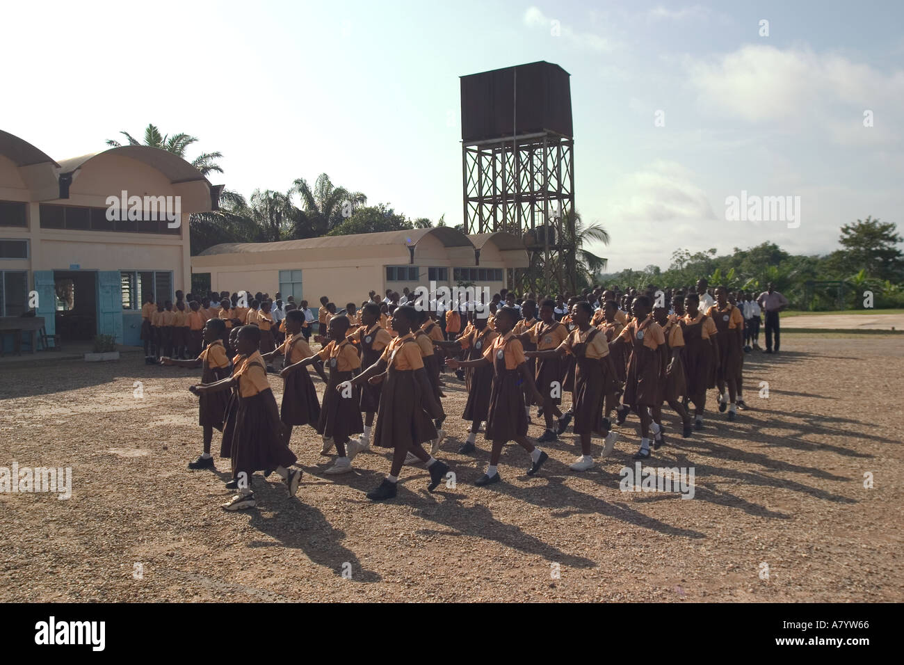 Gruppo misto di bambini delle scuole junior e senior al di fuori della scuola nel parco giochi che marciano e cantano in assemblea e prima delle lezioni In Ghana Africa occidentale Foto Stock
