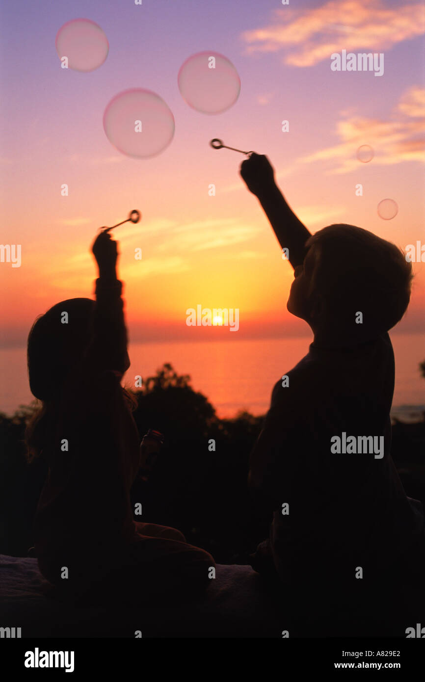 Due bambini di raggiungere per airborne bolle al tramonto Foto Stock