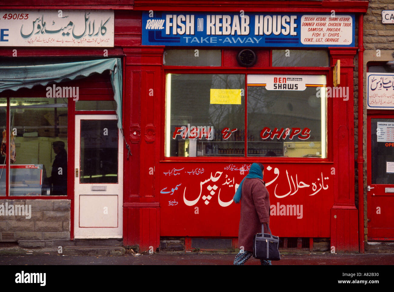 Una donna asiatica passa un pesce e chip shop in Bradford Yorkshire Inghilterra Foto Stock
