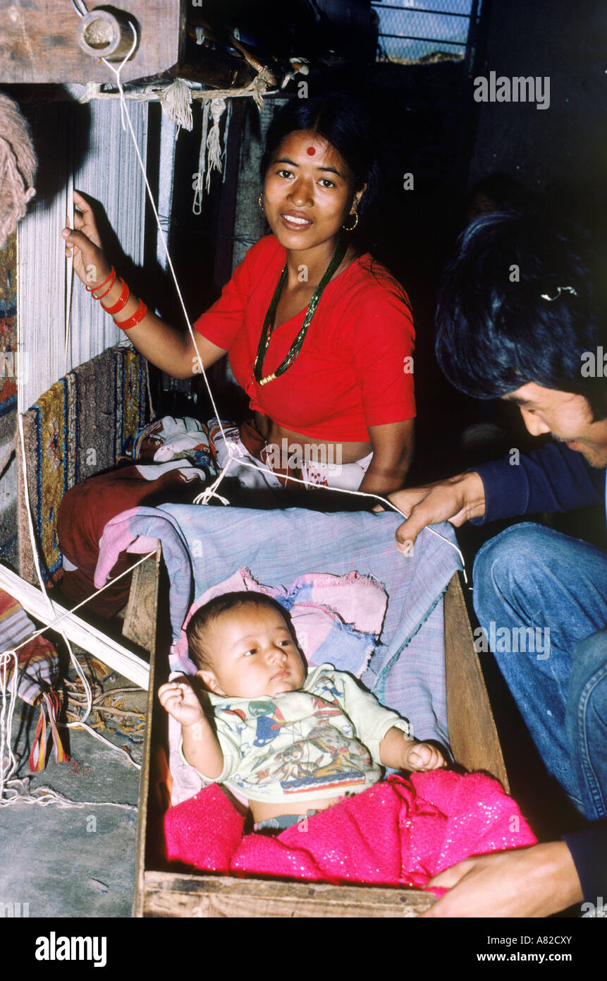 Napalese donna nella fabbrica di tessitura vicino a Katmandu lavorando con telaio mentre la cura per il suo bambino nel bilanciere in legno Foto Stock