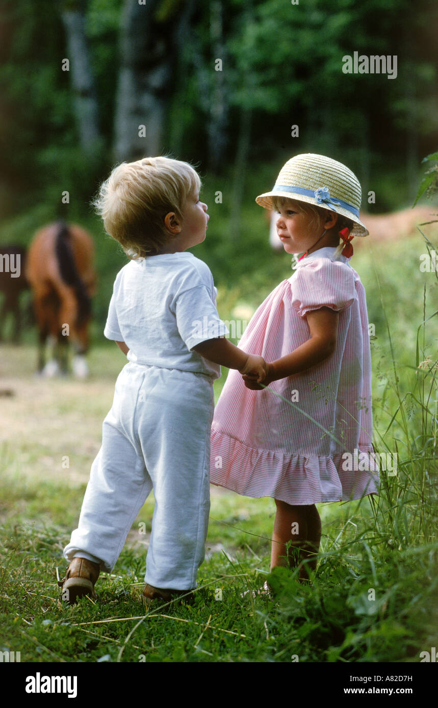 Un ragazzo e una ragazza da 2 a 3 anni di età tenendo le mani in campo con i cavalli Foto Stock