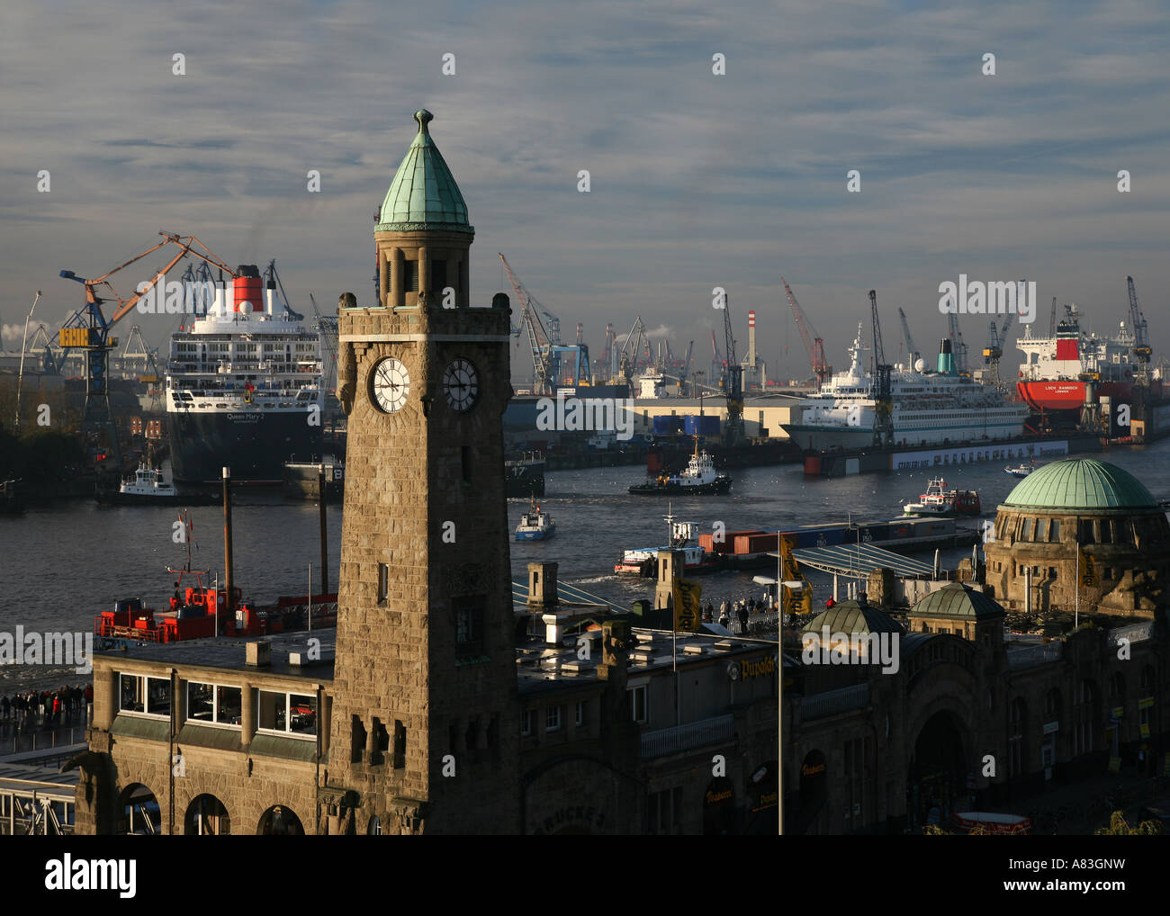 La storica torre dell'orologio di edificio Landungsbruecken e Queen Mary II nel bacino di carenaggio di Blohm + Voss di Amburgo, Germania Foto Stock