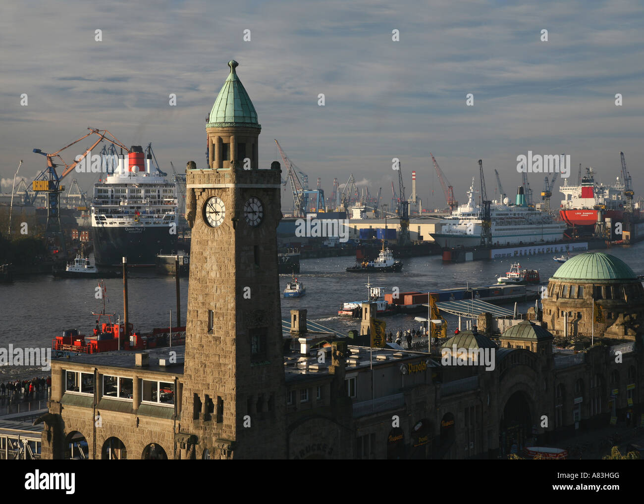 La storica torre dell'orologio di edificio Landungsbruecken e Queen Mary II nel bacino di carenaggio di Blohm + Voss di Amburgo, Germania Foto Stock