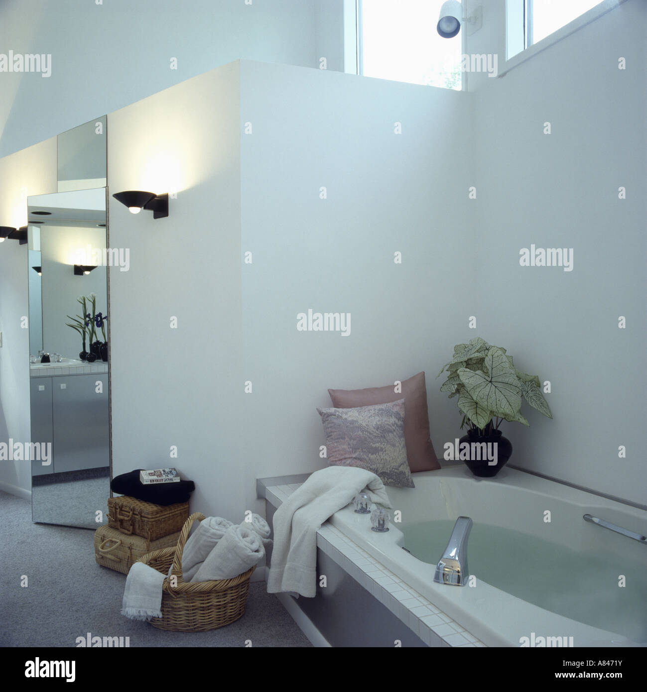 Cuscini sul bordo della vasca da bagno in bianco e moderno bagno con parete illuminata-luci e asciugamani bianchi nel cestello Foto Stock