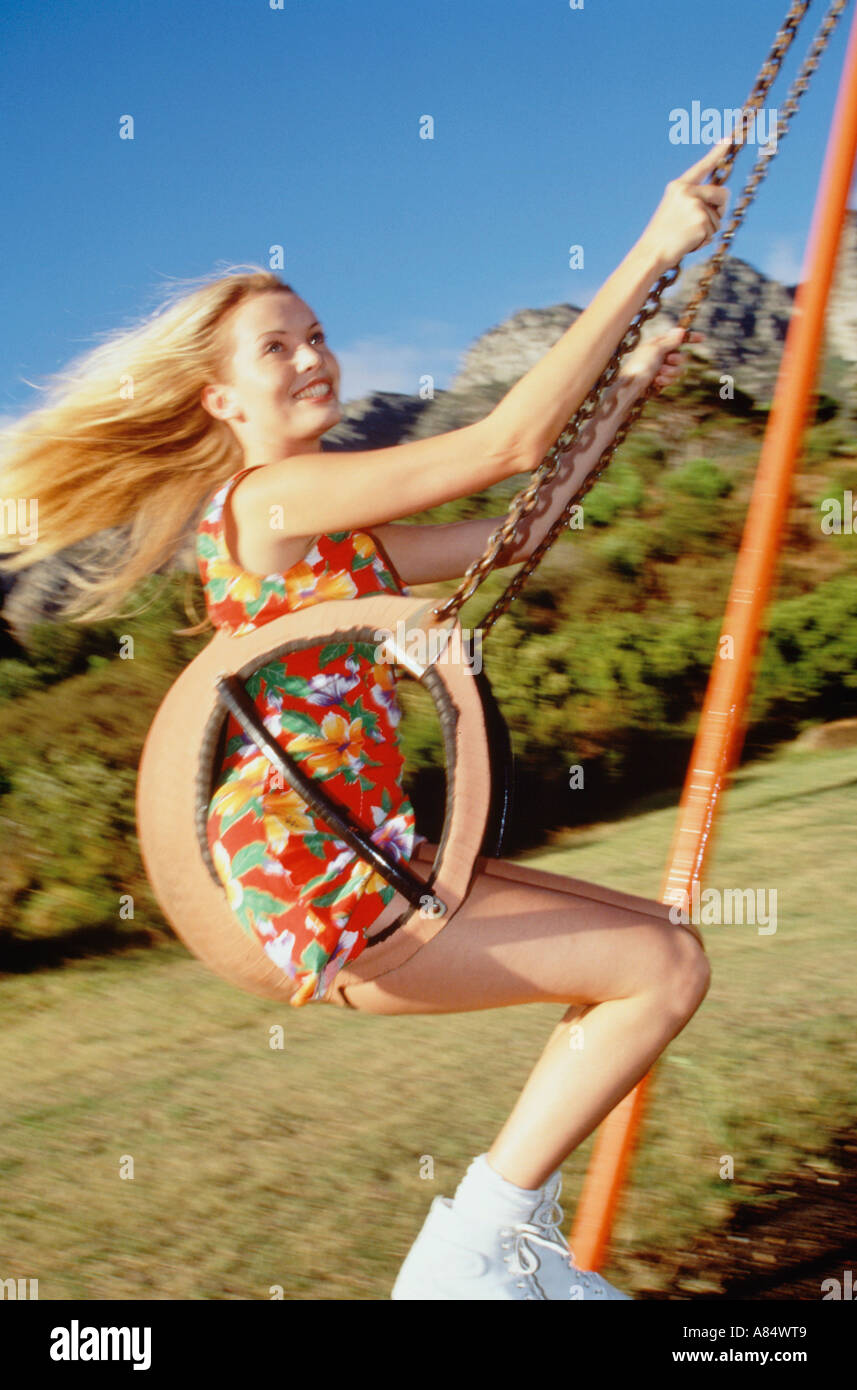 Giovane donna in abiti estivi sul sedile oscillante nel parco giochi per bambini. Foto Stock