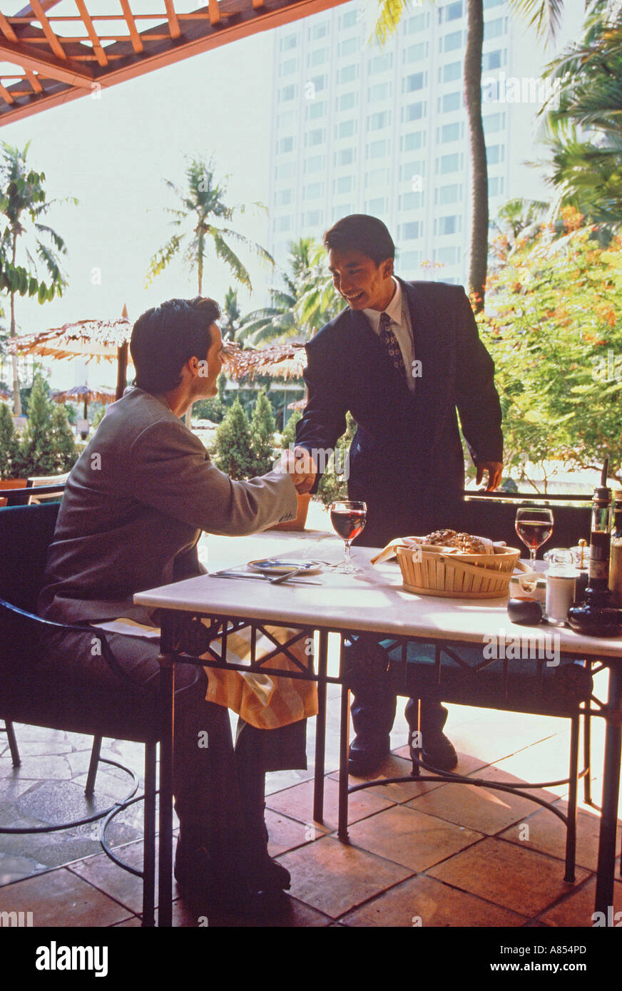 Due uomini handshake saluto sulla terrazza esterna del ristorante di Singapore. Foto Stock