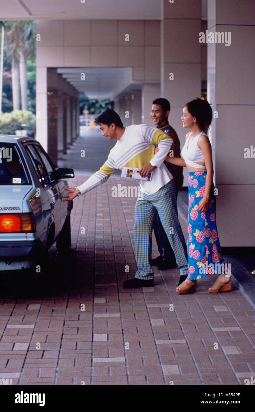 Singapore. Coppia giovane in taxi. Uomo di raggiungere per maniglia per porte di veicoli. Foto Stock