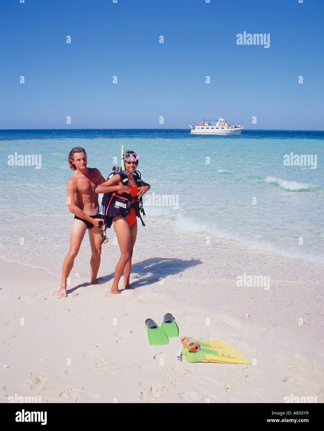 Giovane uomo in costume da bagno aiutando giovane donna in tuffo dello scuba marcia a Beaver Cay, Queensland, Australia. Barca in background. Foto Stock