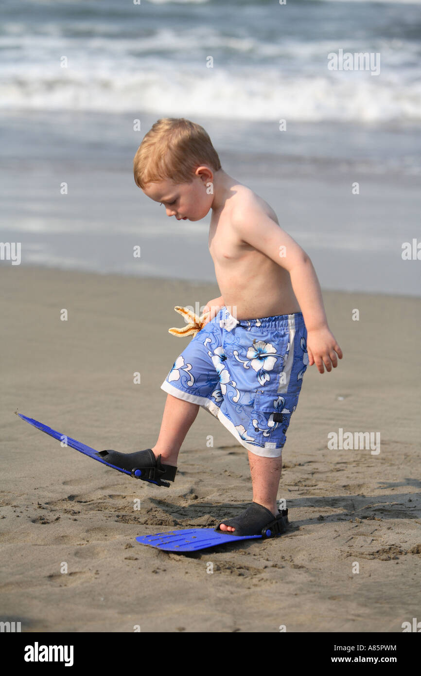 Bimbo di 2 anni a piedi con pinne in spiaggia Foto Stock