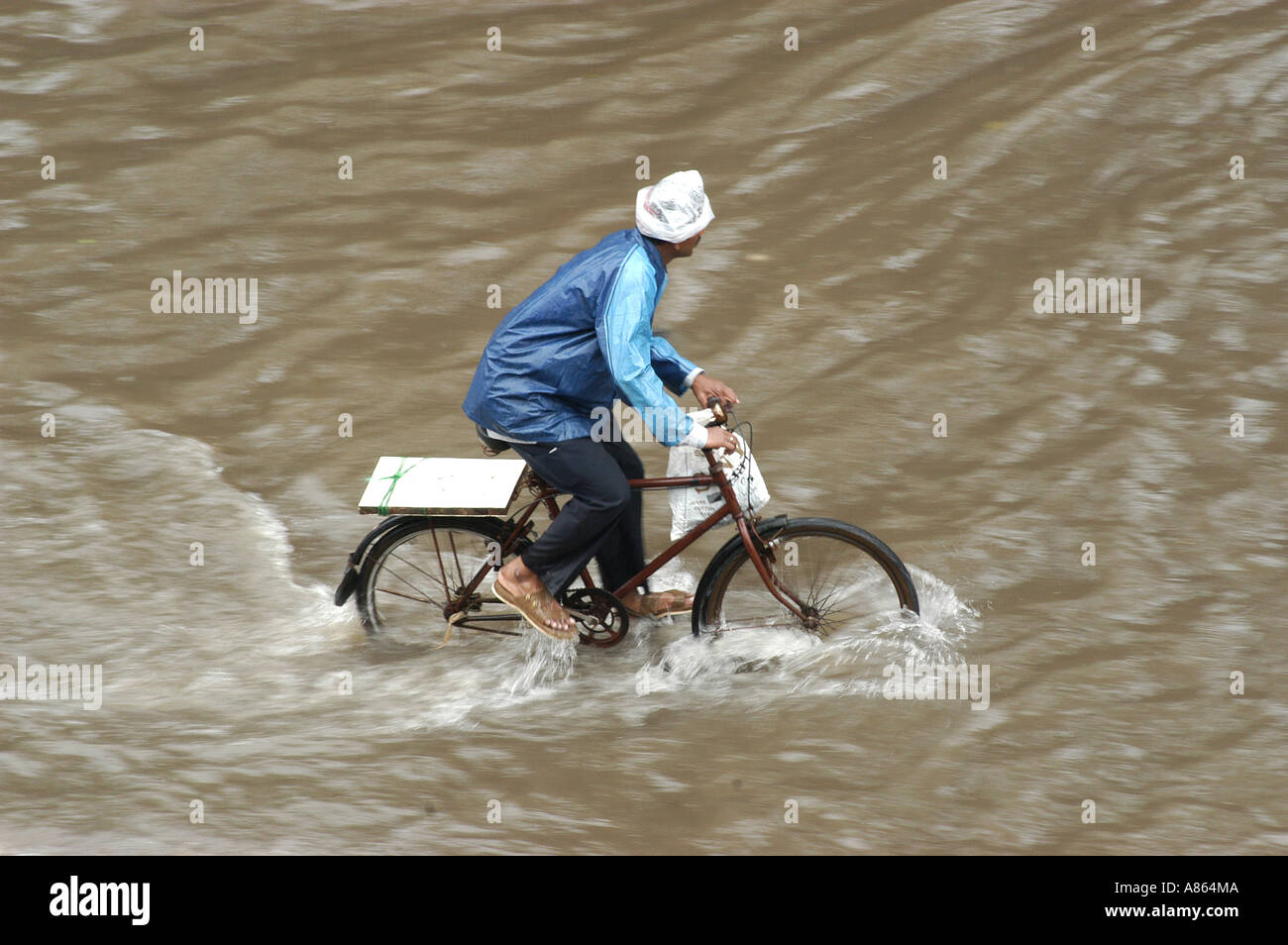 Uomo in impermeabile in bicicletta su monsone pioggia allagato strada Bombay Mumbai Maharashtra India Asia Foto Stock