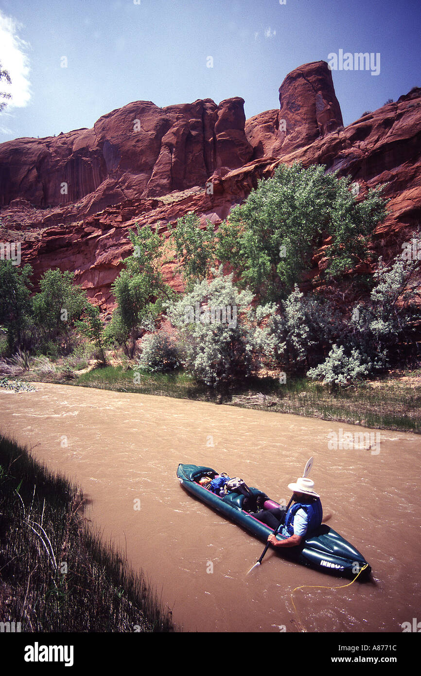 Un uomo solitario di indossare un giubbotto di salvataggio e il cappello in un kayak le righe lungo un fiume fangoso con il Escalantic Monumento Nazionale dietro di lui Foto Stock