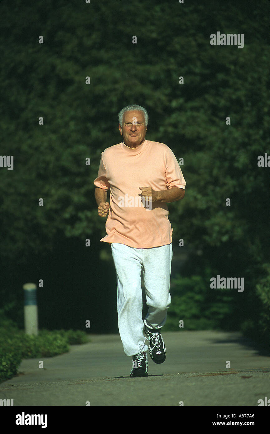 Un sorridente senior citizen maschio 70s 73 anni anni di indossare pantaloni di sudore orange t shirt jogging giù un percorso in un parco Caucasian POV SIGNOR ©Myrleen Pearson Foto Stock