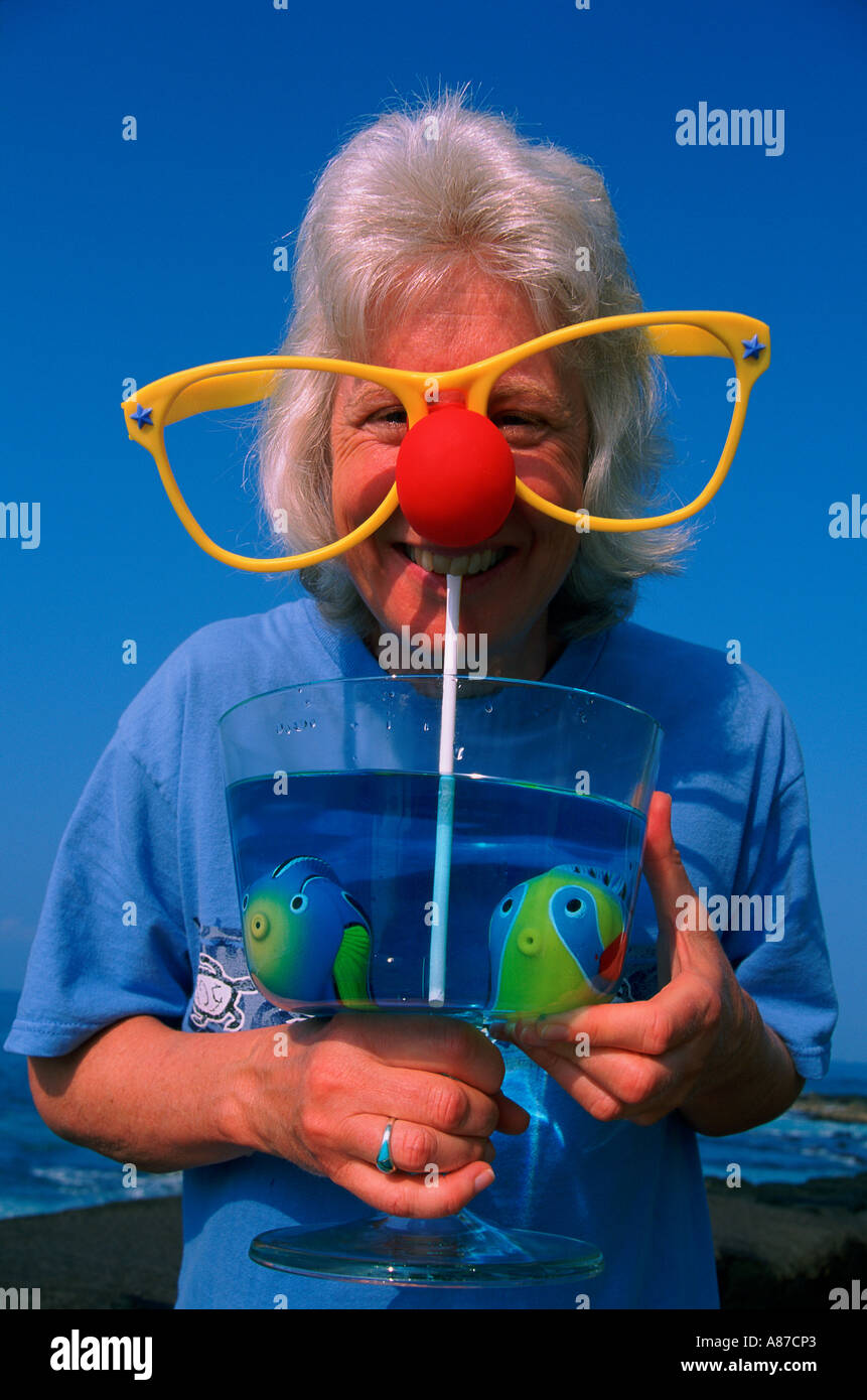 Una donna di mezza età che indossa grandi bicchieri da clown e sorseggiate un bicchiere di plastica finto pesce prelevato in Kona Hawaii Foto Stock