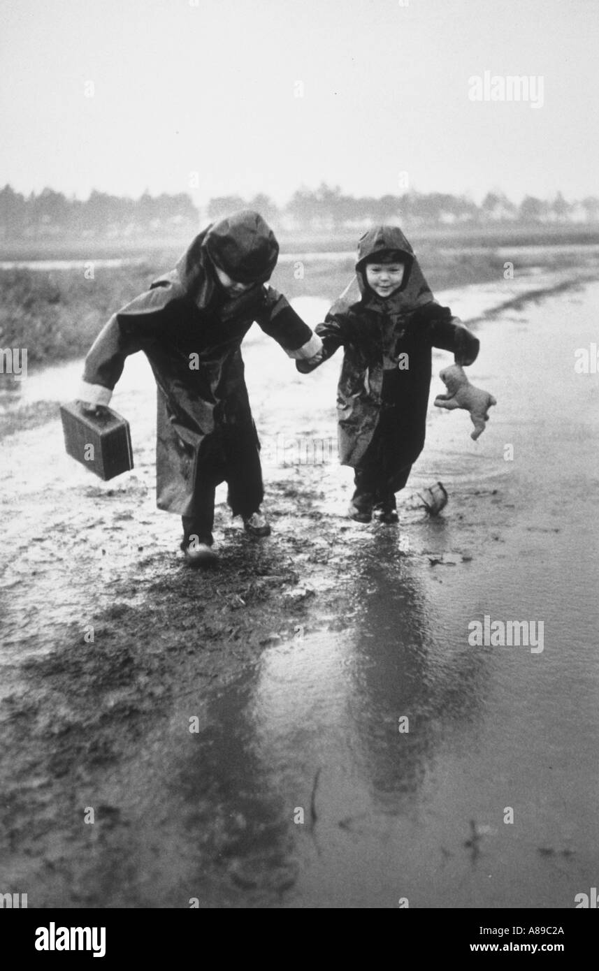 Due giovani fratelli indossando oscura pioggia slickers saltare in pozze mentre si cammina a scuola insieme Foto Stock