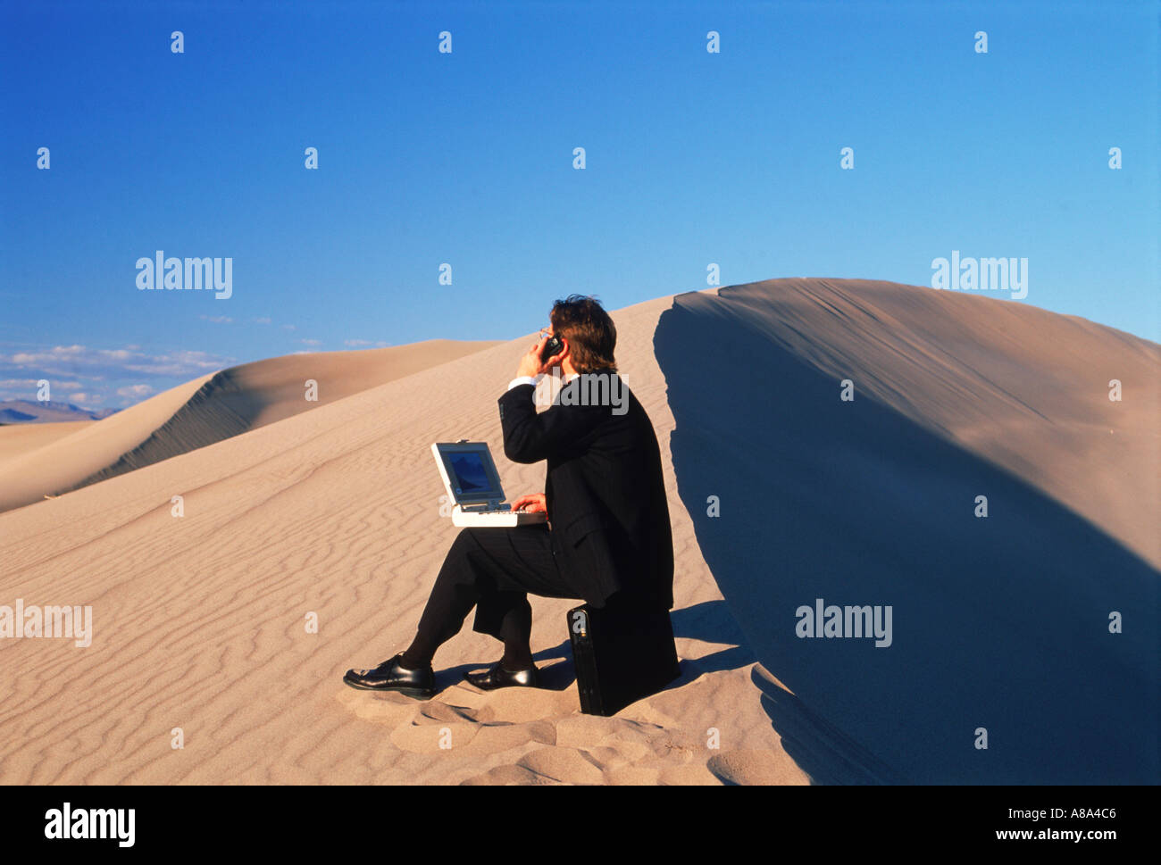 Imprenditore nel deserto con computer portatile parlando al cellulare nel suo ufficio per esterni Foto Stock