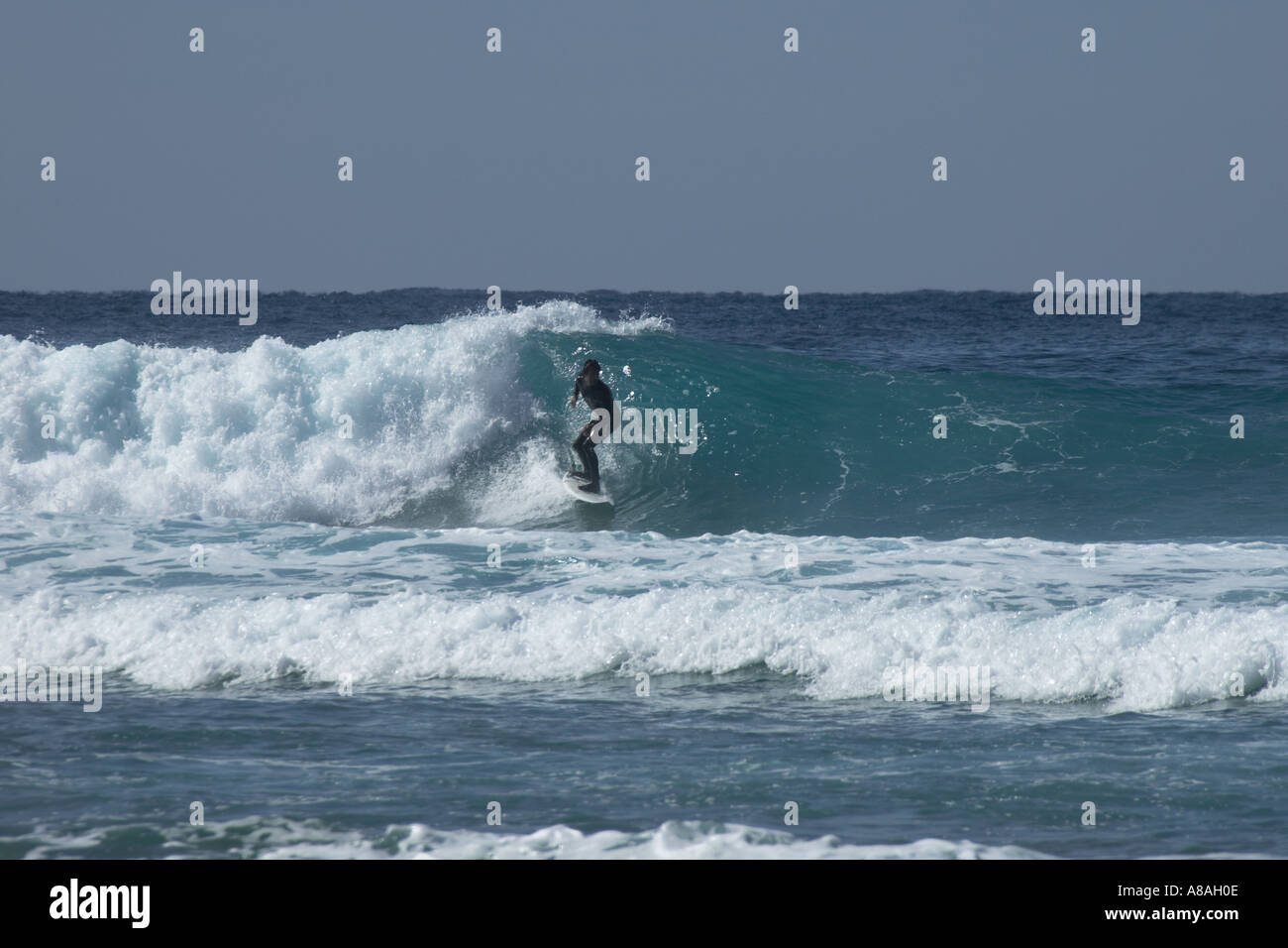 Surfista solitario cavalca un potente onda atlantico su una spiaggia di Algarve metà mattina Foto Stock