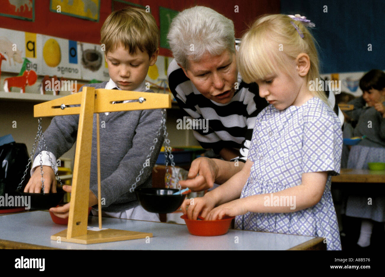 Insegnante aiutando i bambini a Londra scuola preparatoria per pesare oggetti su scale Foto Stock