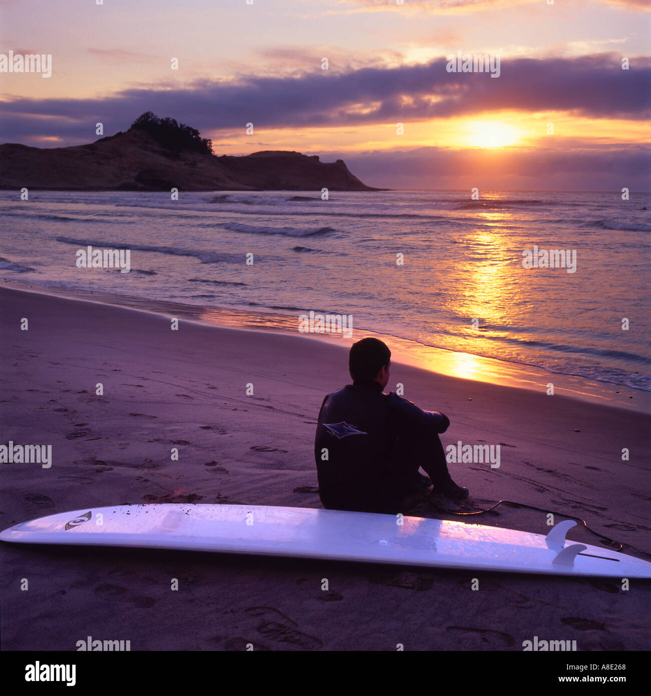 Surfer seduto sulla spiaggia al tramonto Foto Stock