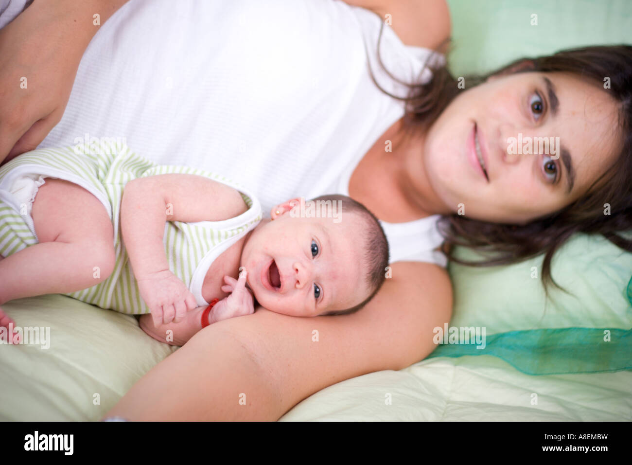 Giovane donna con il suo bambino sorridente adagiato su un letto Foto Stock