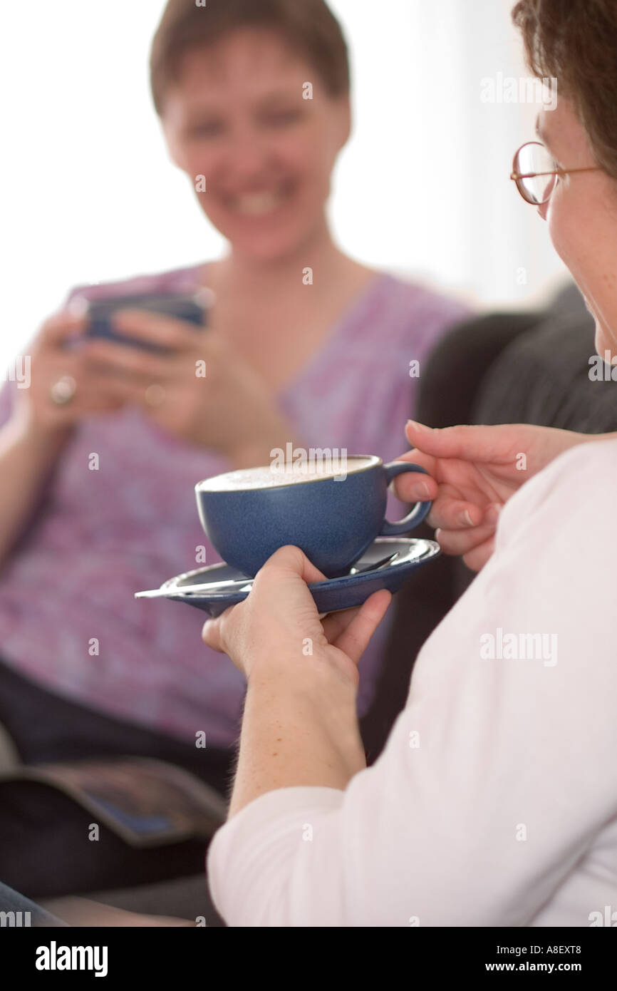 Le donne rilassante e chiacchierando con tazze di caffè a casa REGNO UNITO Foto Stock