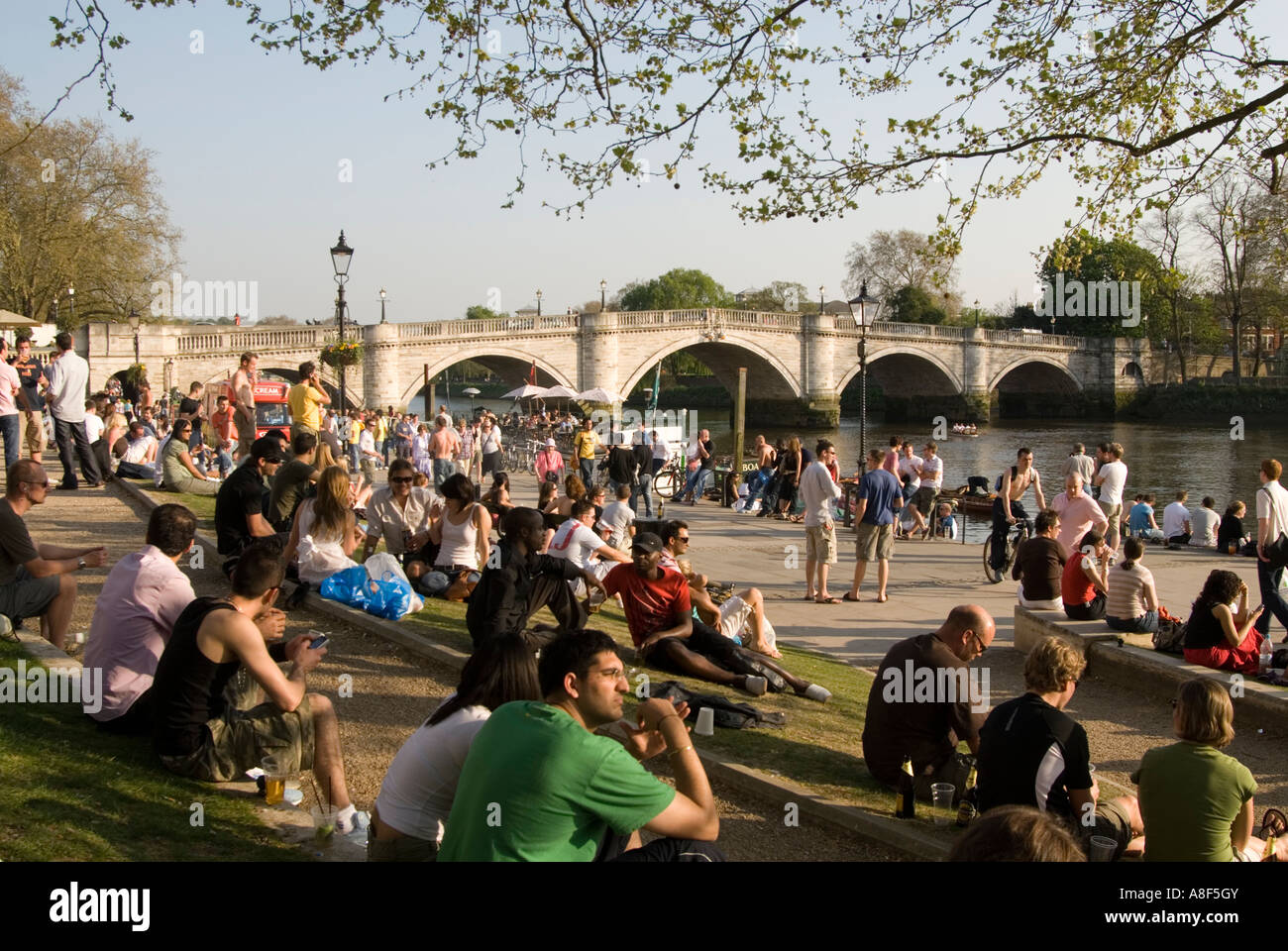 Persone rilassante sulla riva del fiume Tamigi accanto a Richmond Bridge, Londra Inghilterra REGNO UNITO Foto Stock