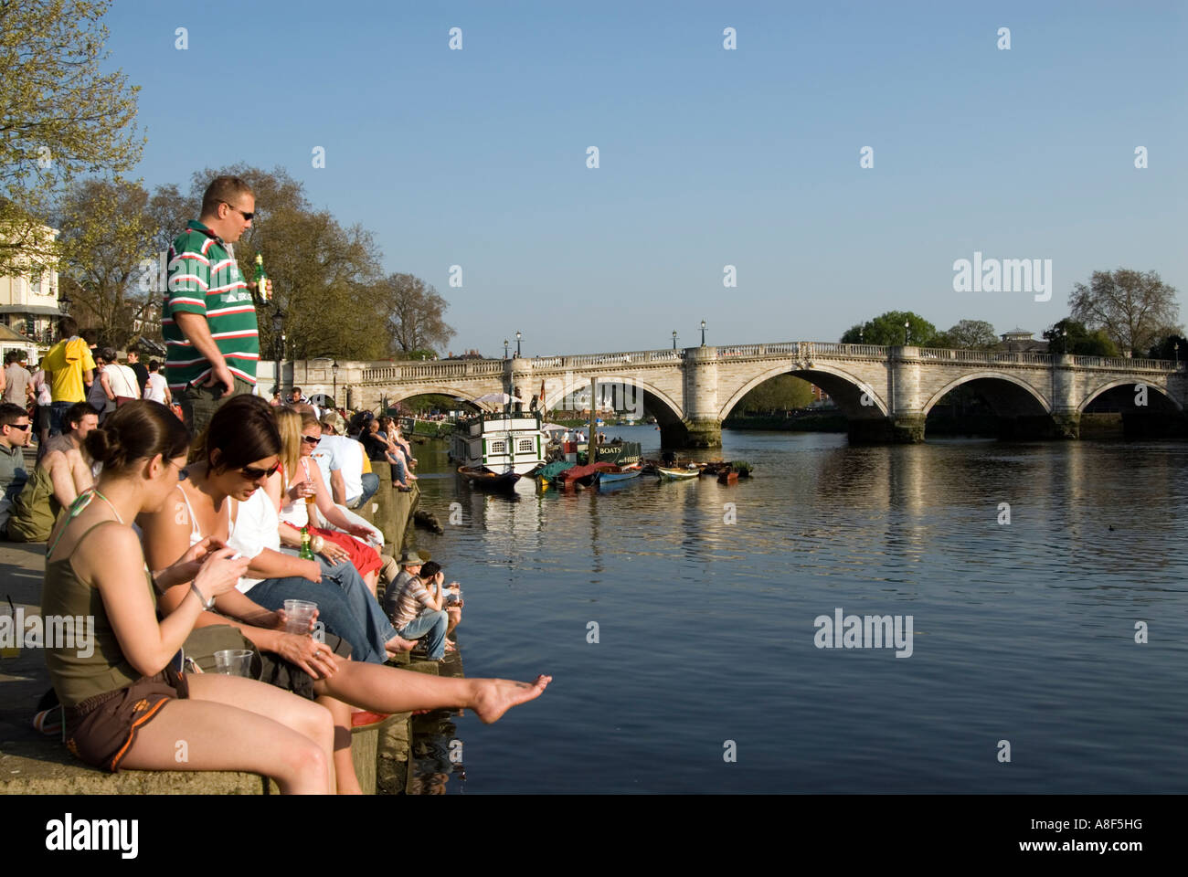 Persone rilassante sulla riva del fiume Tamigi accanto a Richmond Bridge Londra Inghilterra REGNO UNITO Foto Stock