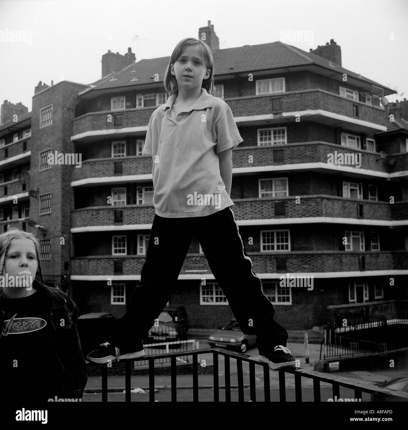 Una giovane ragazza si erge sulla ringhiera che circonda il suo alloggiamento del consiglio station wagon, Clapton, Londra, Regno Unito. Foto Stock