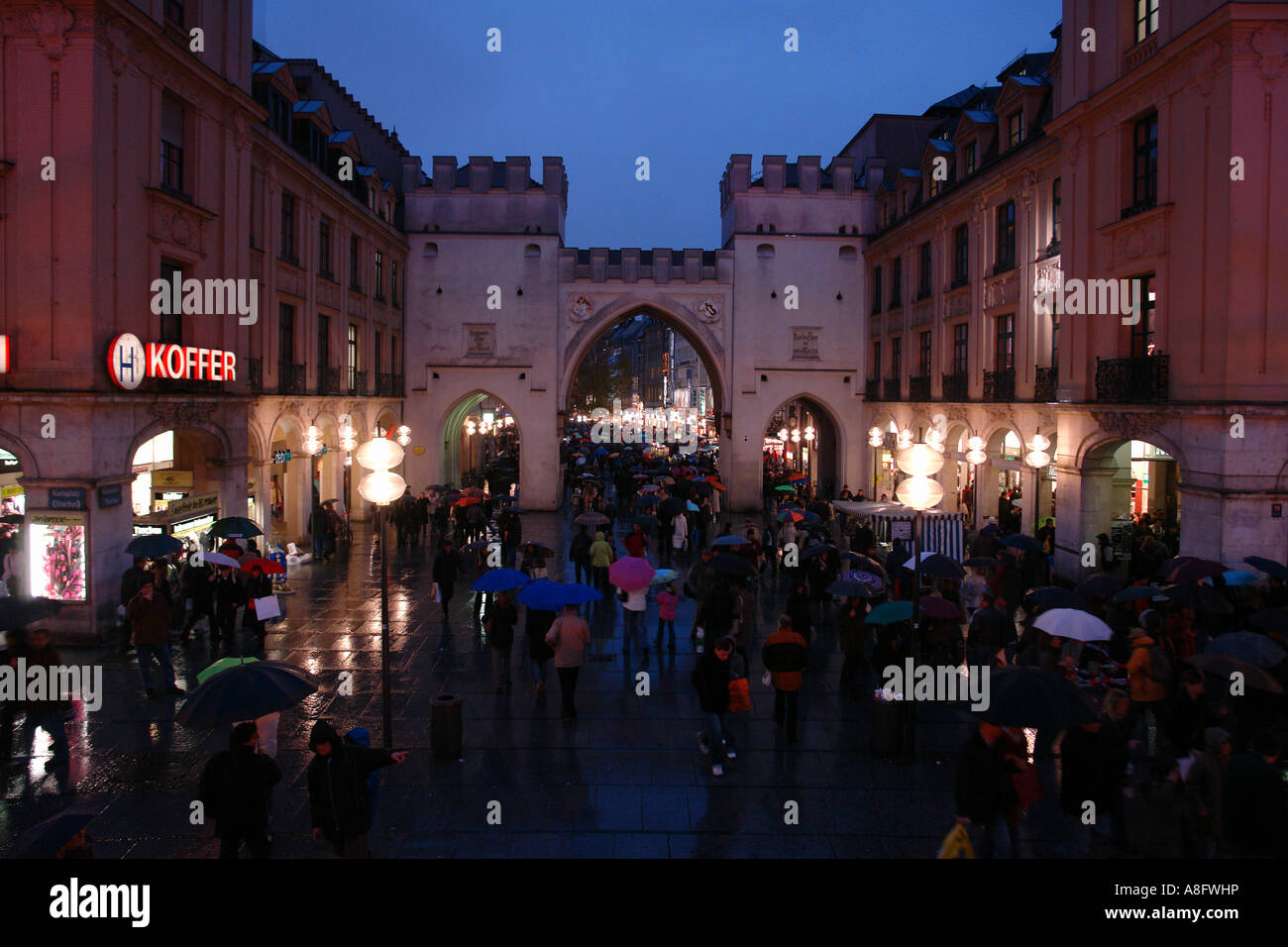 Pedoni con ombrelloni a piedi attraverso Karlstor al crepuscolo Karlsplatz Stachus Monaco di Baviera Baviera Germania Foto Stock