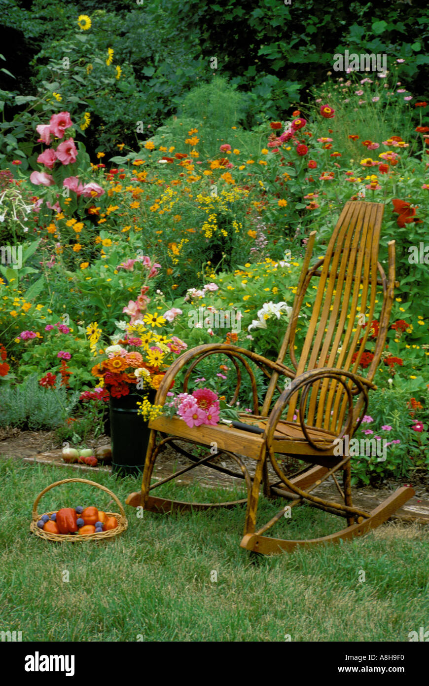 Dalle due nonne luogo-- Bentwood sedia a dondolo nel giardino fiorito con un tessuto cesto pieno di frutta fresca e fiori freschi recisi Foto Stock