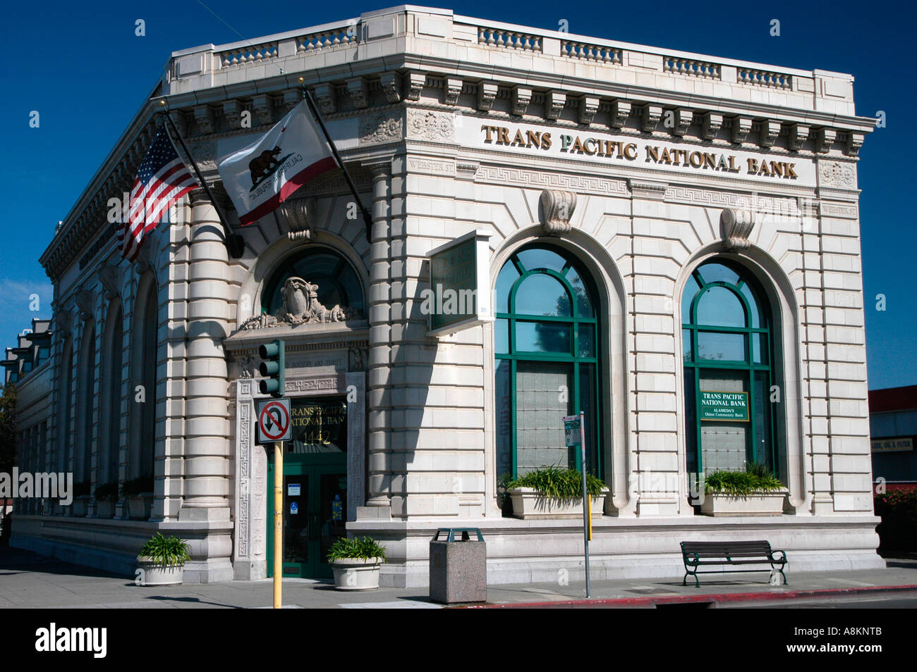 Trans Pacific National Bank, un edificio storico di una banca in pietra ad Alameda, California, con bandiere degli Stati Uniti e della California che sventolano davanti Foto Stock