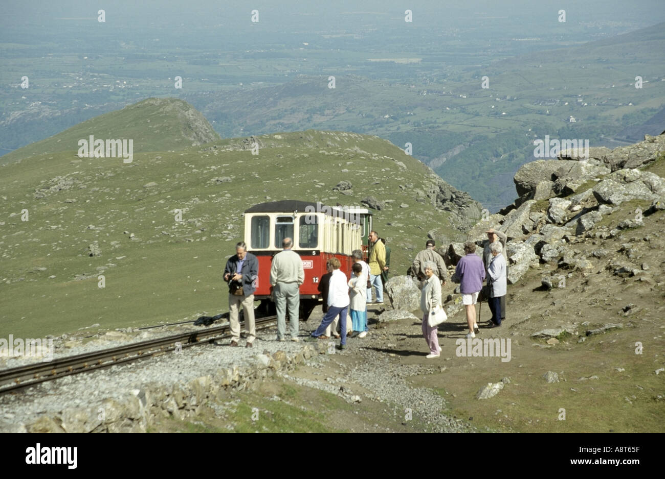 Treno di montagna Snowdon e passeggeri in visita turistica che aspettano di rientrare a bordo a metà strada con Snowdonia Gwynedd North Wales UK paesaggio oltre Foto Stock