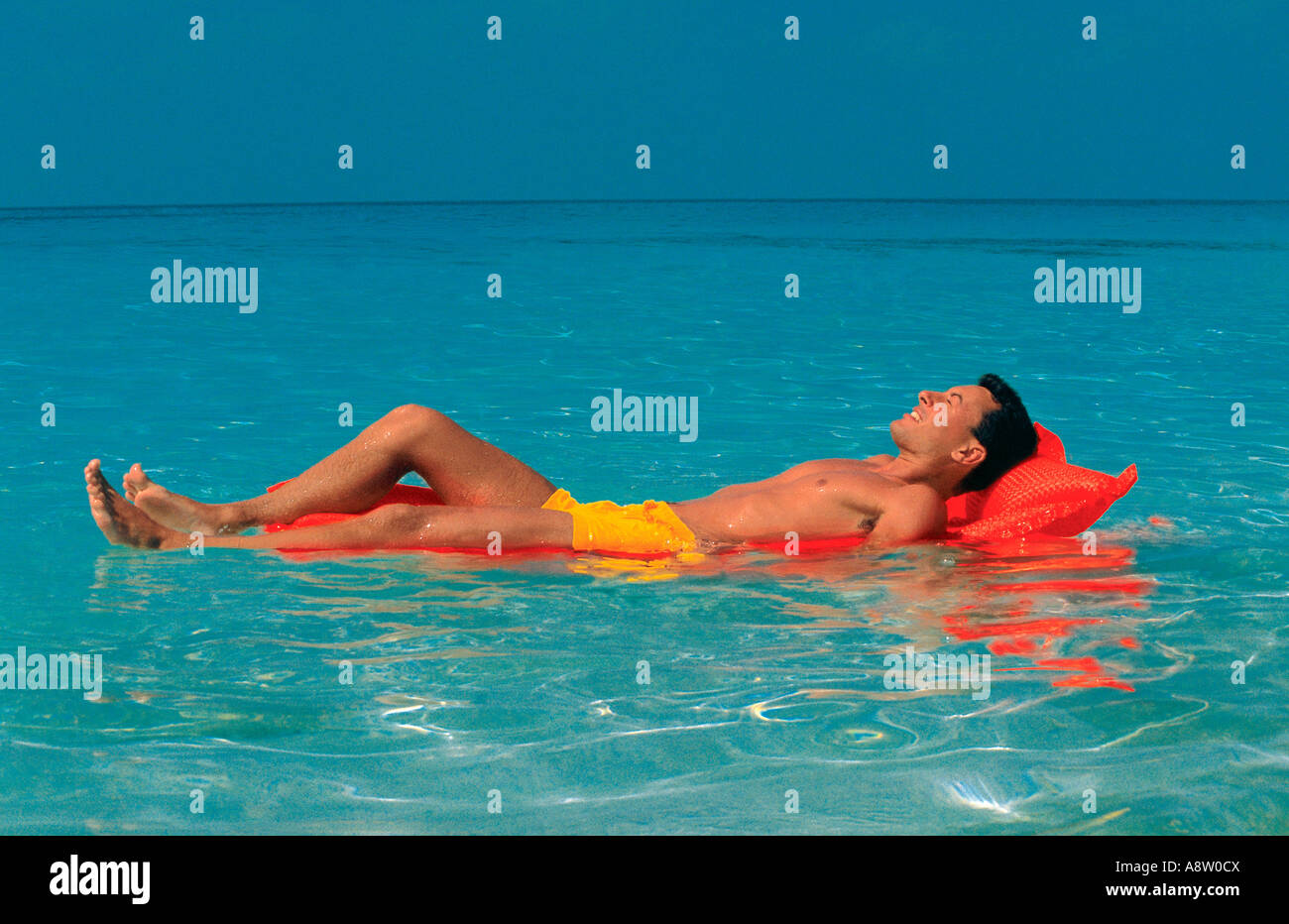Maldive. Giovane uomo in costume da bagno sul letto aria galleggianti su acqua cristallina. Foto Stock