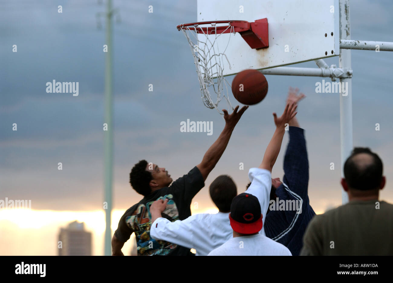 Un gruppo di uomini giocano a basket come il sole tramonta su prevalentemente ispanico Fair Haven quartiere di New Haven Foto Stock