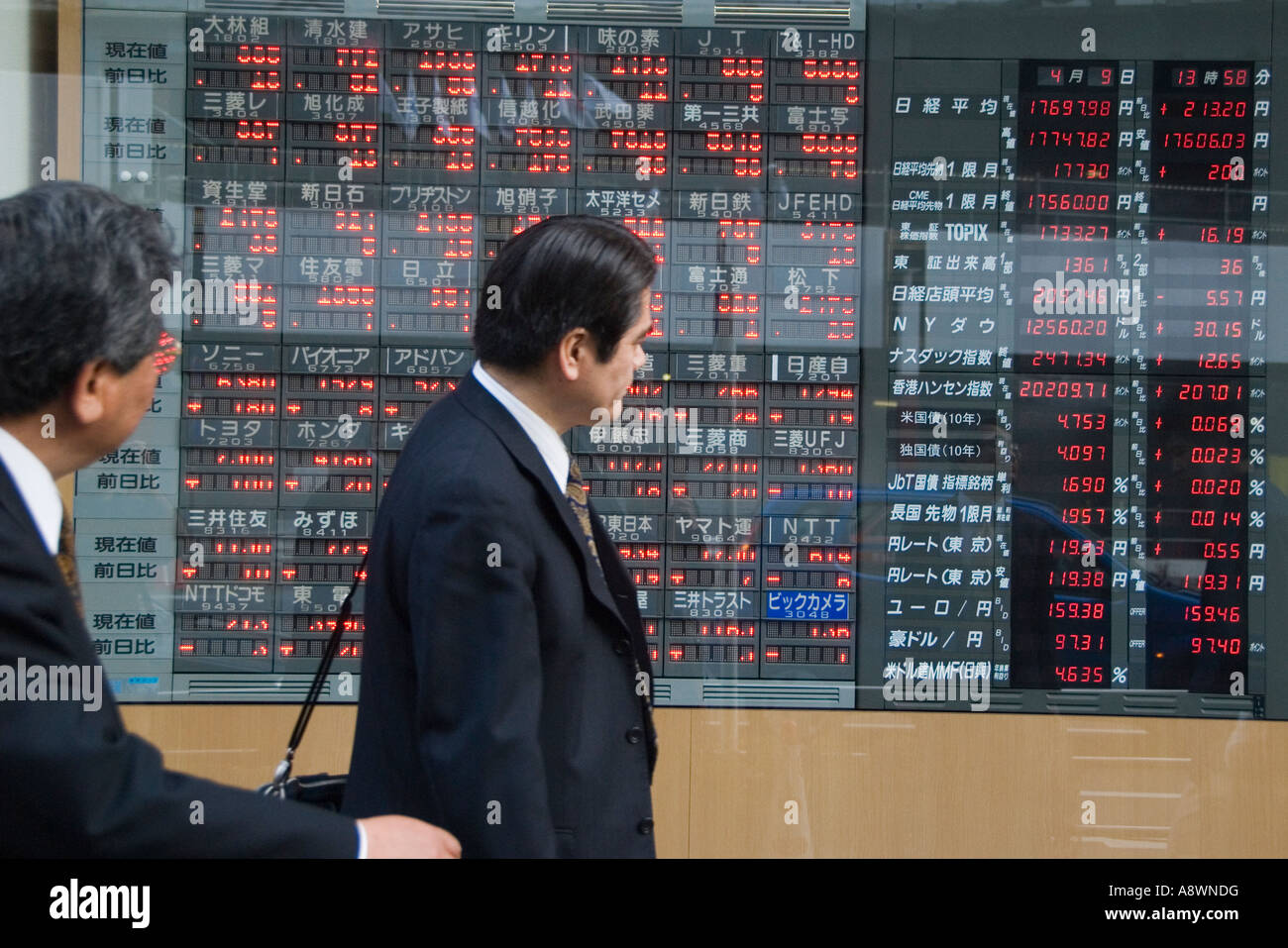 Due imprenditori a piedi da un consiglio di amministrazione che mostra le quotazioni di borsa di Tokyo Giappone Foto Stock