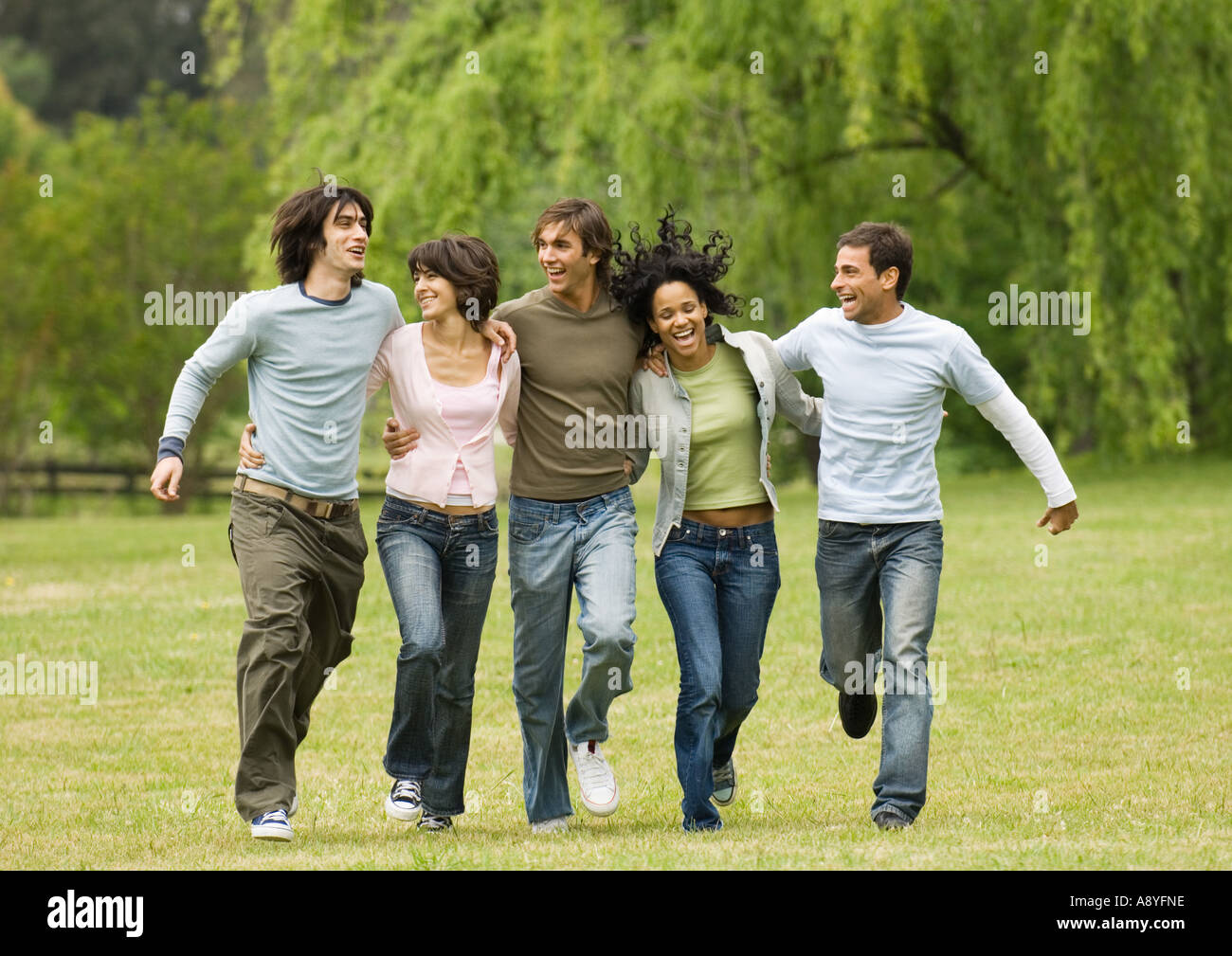 Un gruppo di giovani amici con le braccia intorno a ciascun altro, saltando su tutto il campo Foto Stock Un gruppo di giovani amici con le braccia intorno a ciascun altro, saltando su tutto il campo Foto Stock