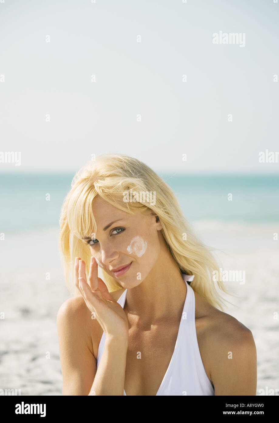 Donna l'applicazione di crema solare a faccia sulla spiaggia Foto Stock