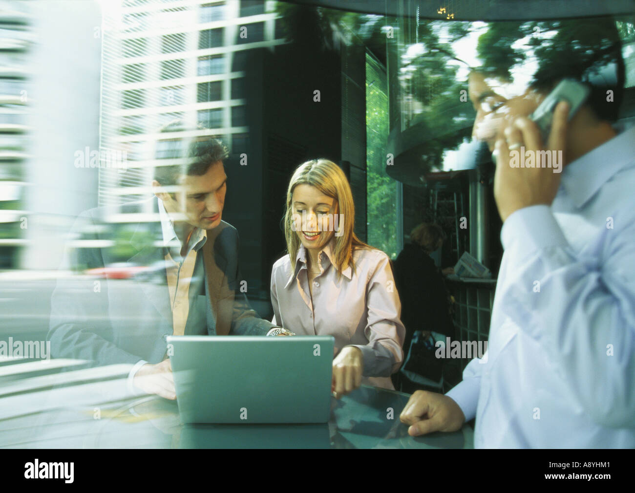 Imprenditore e imprenditrice utilizzando laptop mentre il secondo uomo utilizza il telefono cellulare Foto Stock