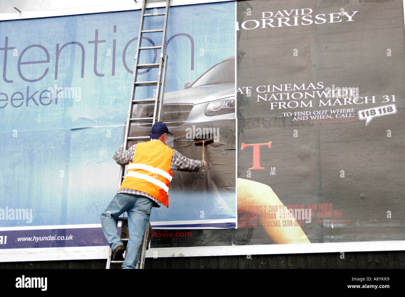 Un lavoratore di sesso maschile paste di un nuovo annuncio di un cartellone Foto Stock