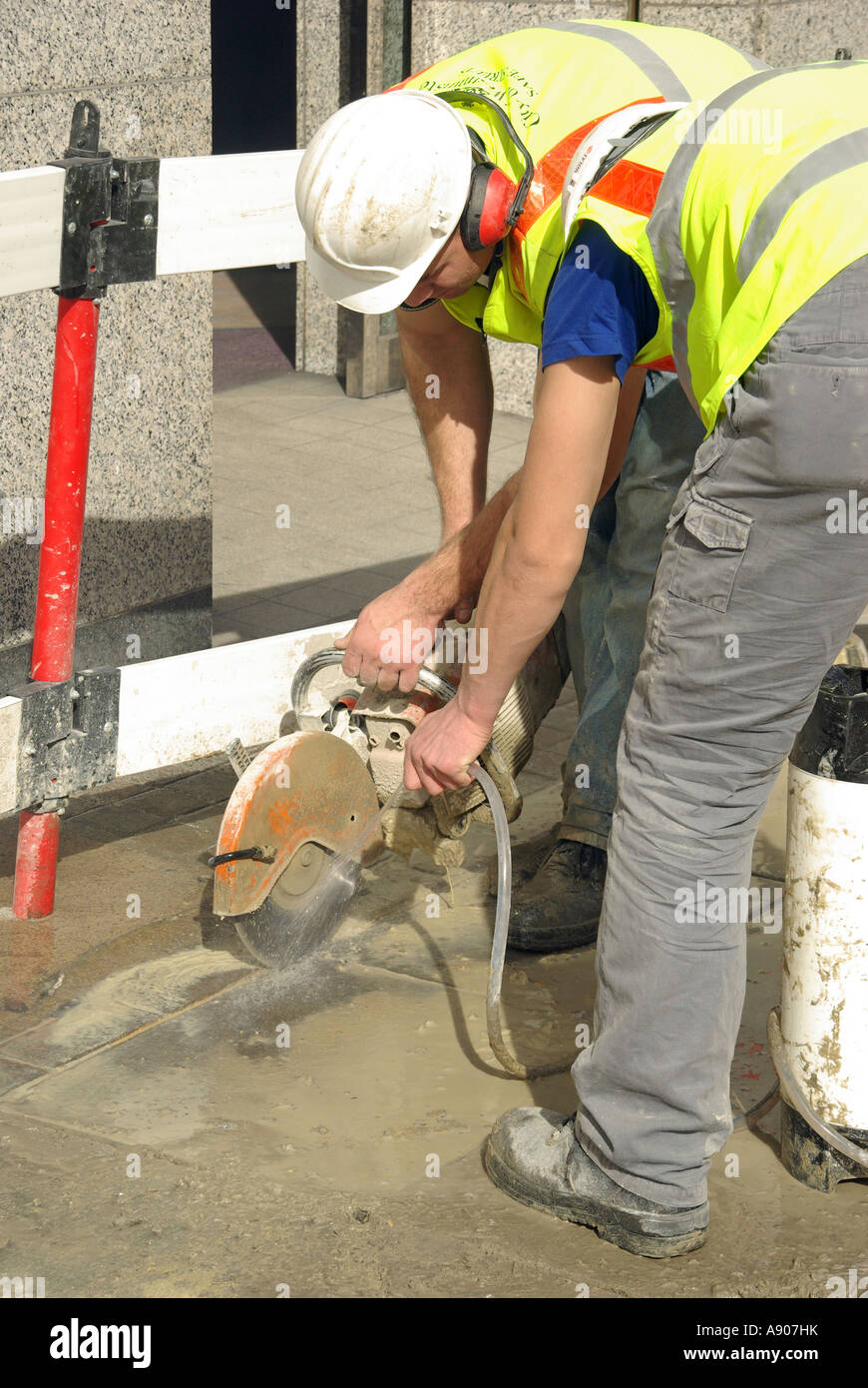 La pavimentazione di stabulazione di riparazione lavori in corso due operai con disco di taglio & water spray per inumidire il controllo verso il basso e la polvere Foto Stock