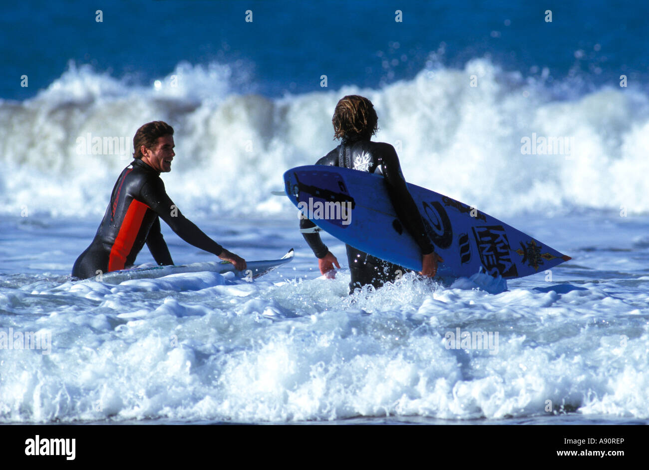 Due surfisti in muta andando per mare a cavalcare le onde che trasportano i loro tavole da surf Foto Stock