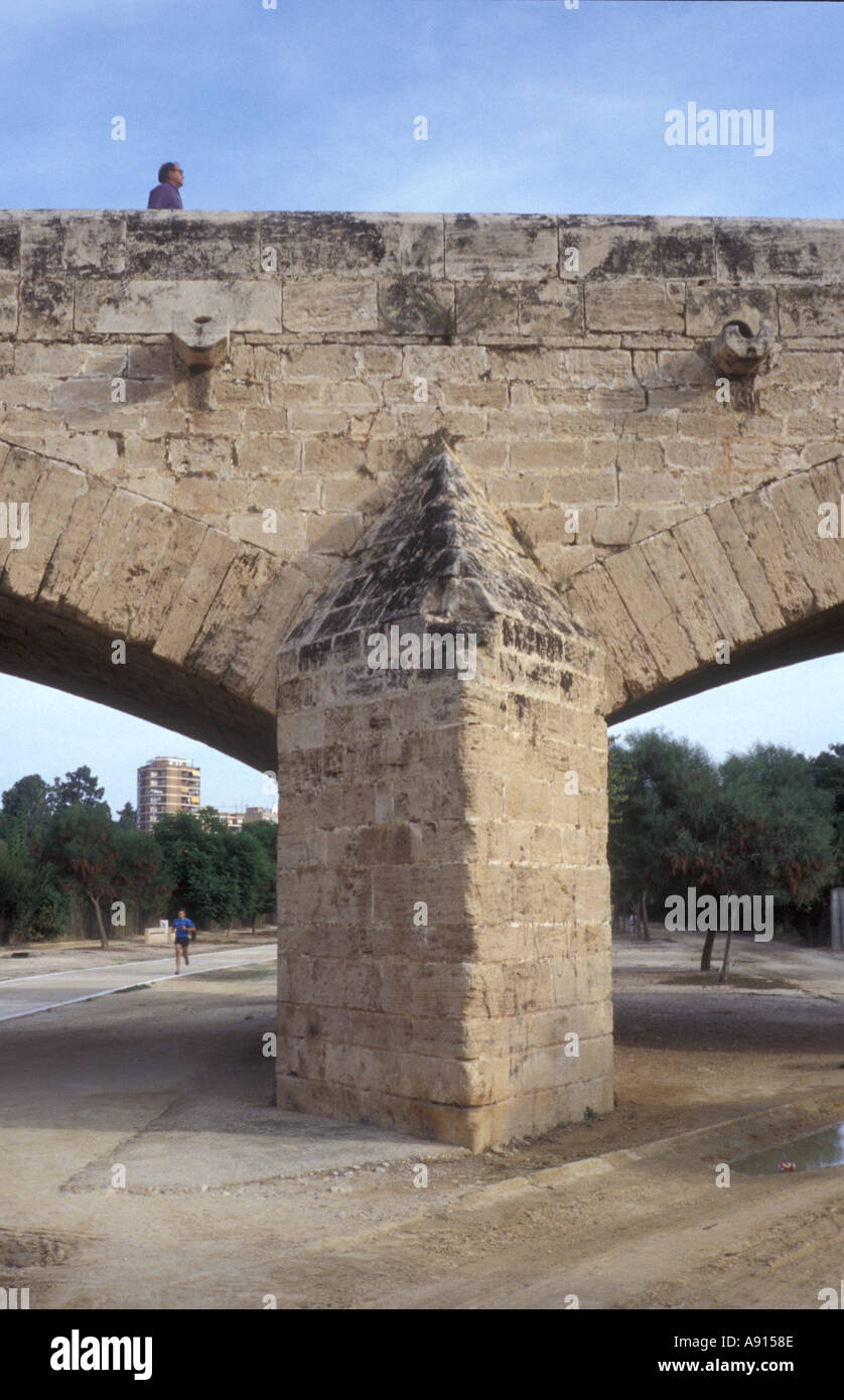 Uomo che cammina oltre il ponte con il passaggio del pareggiatore nel vecchio letto del fiume sotto la domenica sera LOCATION Jardin del Turia Valencia Spagna Foto Stock