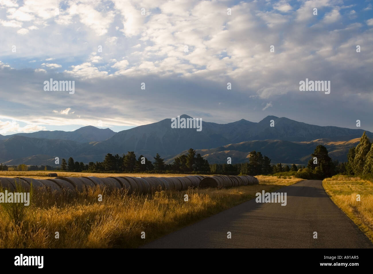 Una strada bagnata in golden sera conduce alla luce del sole fino a sud delle Alpi sull'Isola Sud della Nuova Zelanda Foto Stock