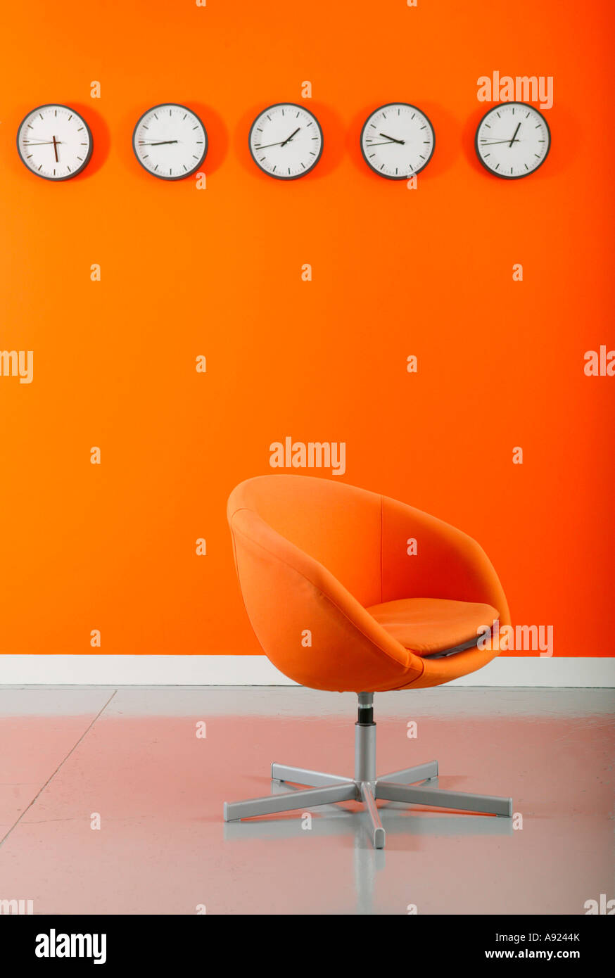 Sedie di colore arancione nella parte anteriore di una fila di orologi su  una parete arancione Foto stock - Alamy