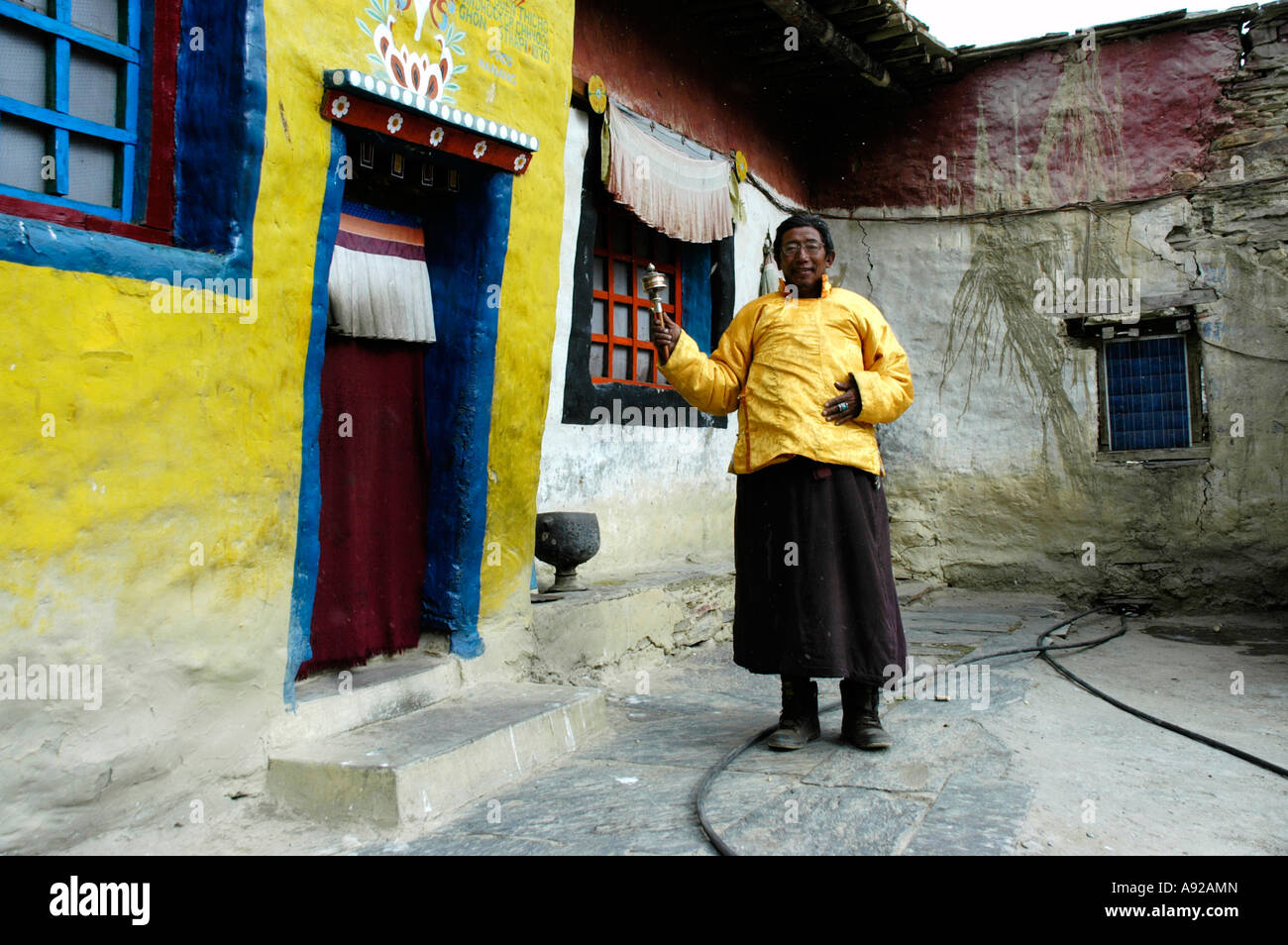 Monaco Lama Sonom vestito in un giallo cape girare una ruota di preghiera nella parte anteriore del monastero di Tashi Gompa Phu Nar-Phu Annapurna Regione Foto Stock