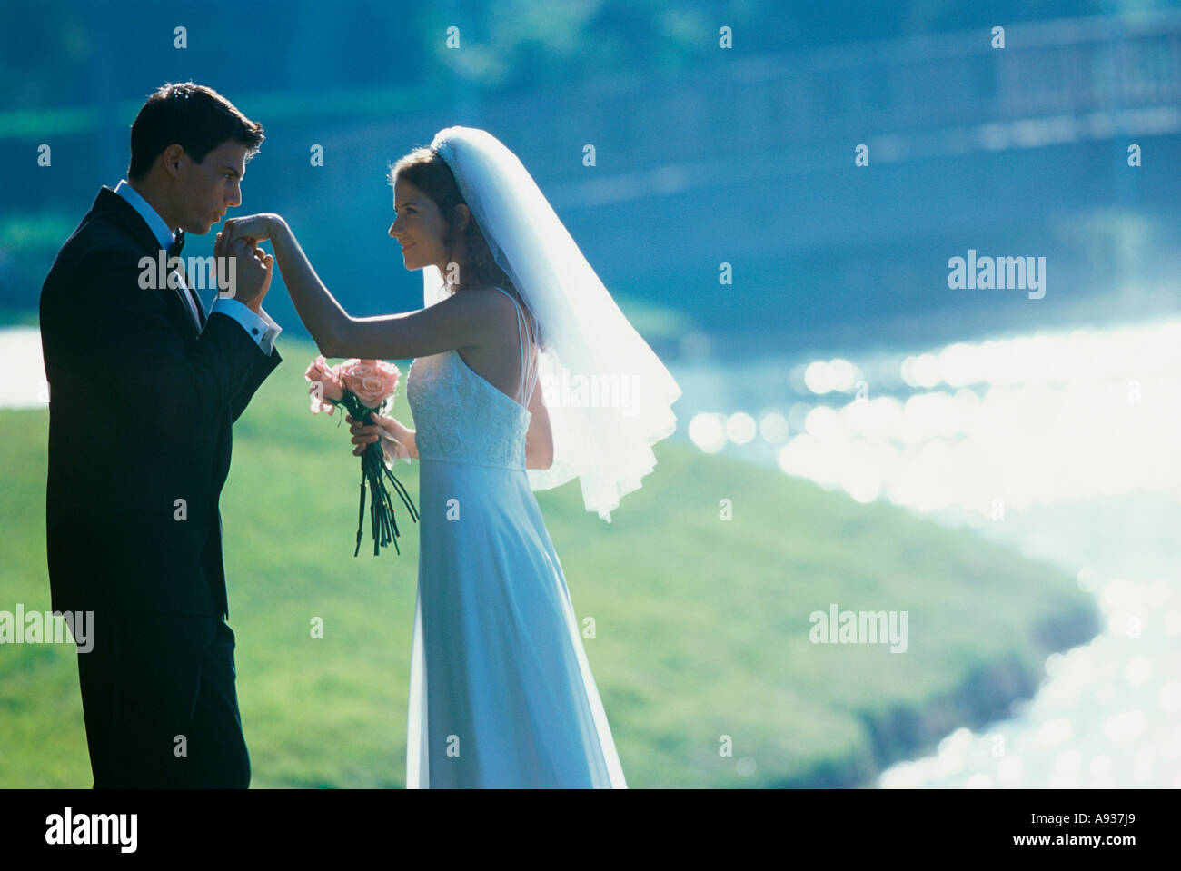 Il profilo laterale di uno sposo baciare la sua sposa la mano vicino a un lago Foto Stock