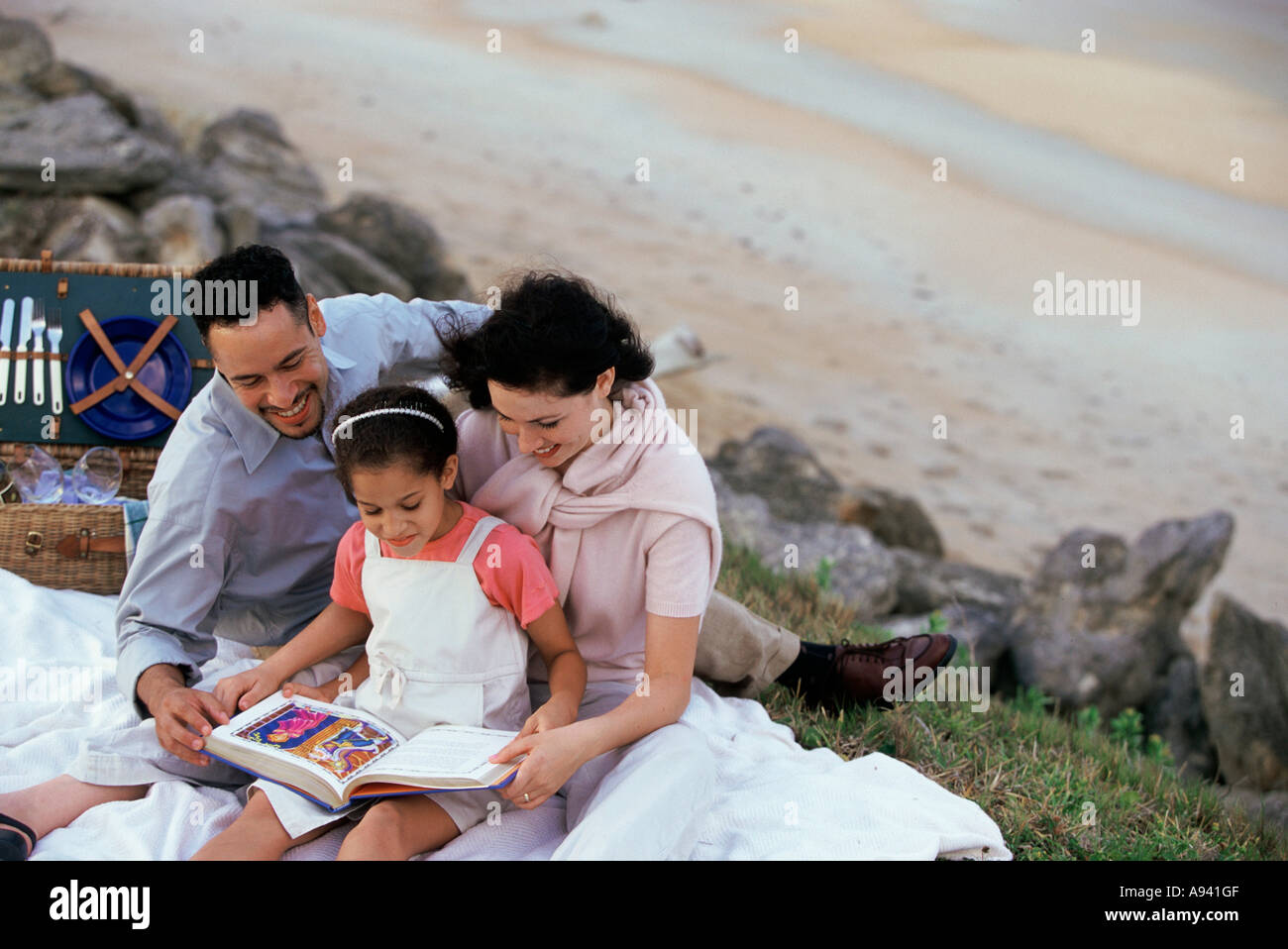 Coppia giovane e la loro figlia la lettura di un libro sulla spiaggia Foto Stock