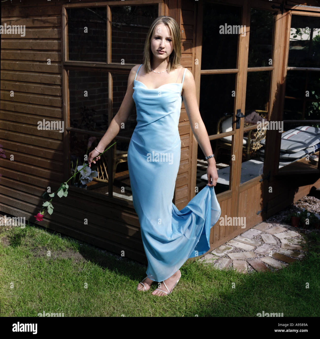 Ritratto di un inglese un adolescente in una lunga veste blu e tenendo una rosa rossa che sta per andare al suo college Prom Foto Stock