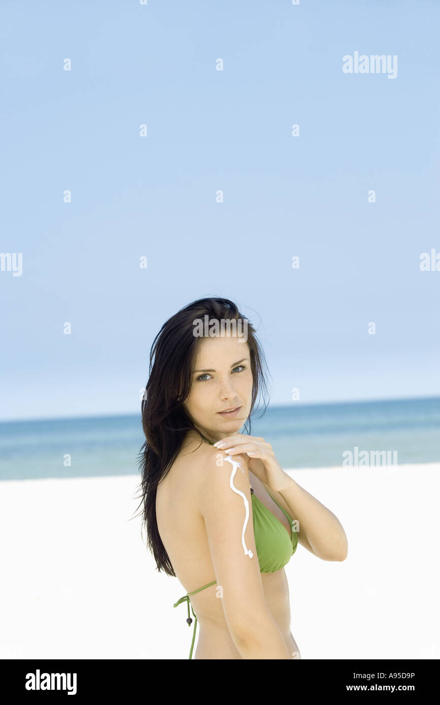 Donna l'applicazione di crema solare al braccio sulla spiaggia, vista laterale Foto Stock