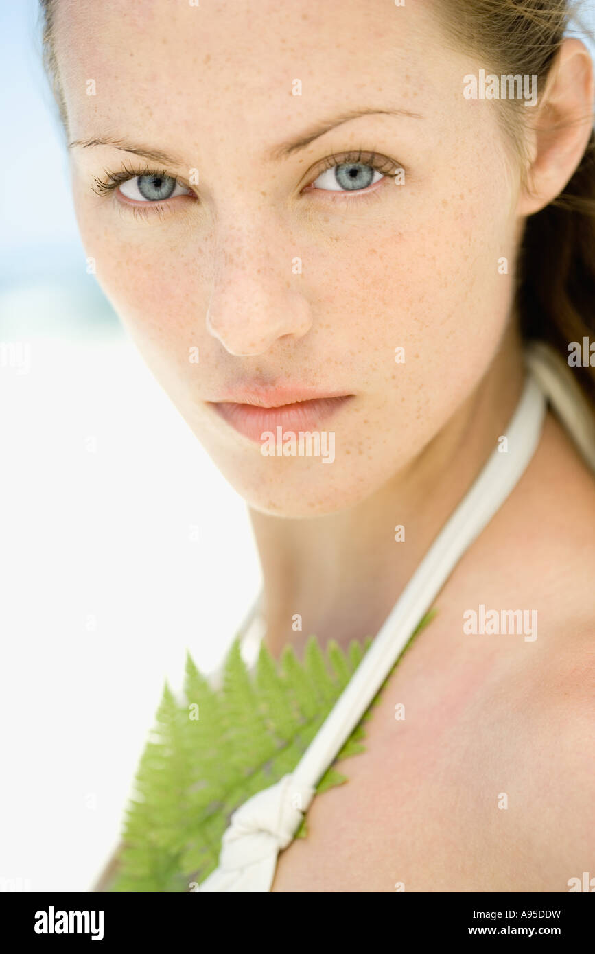 Donna che indossa halter top costume da bagno, foglia contro il petto, guardando la telecamera, close-up, ritratto Foto Stock